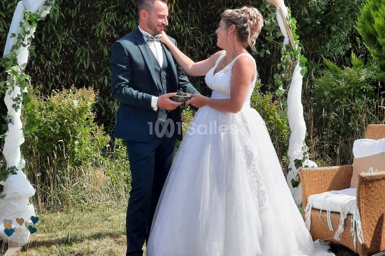 Un couple en tenue de mariage échange un moment tendre sous une arche décorée dans un jardin.