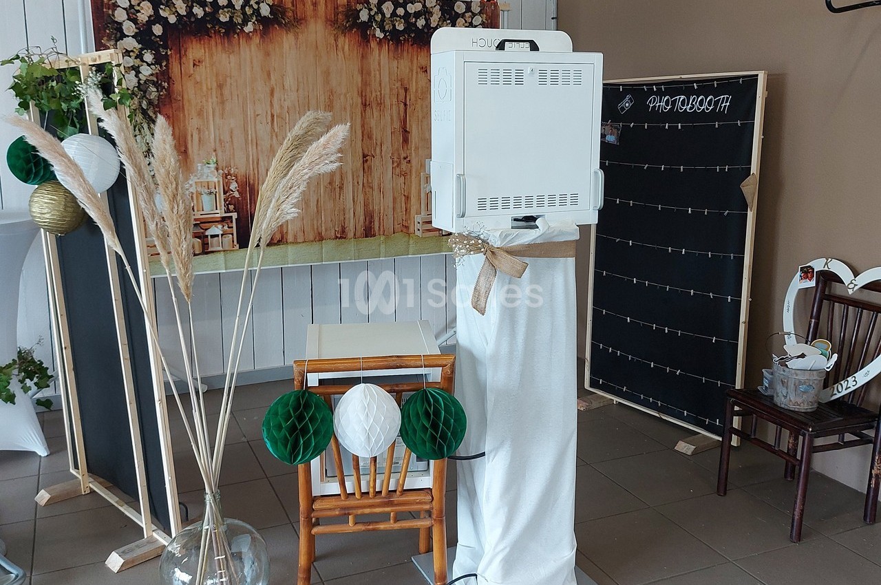 Photobooth installé dans un espace décoré avec des éléments naturels, un fond en bois et des accessoires festifs.