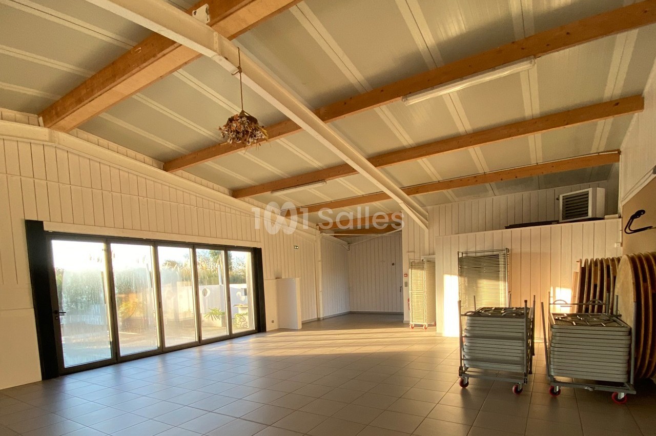 Salle lumineuse avec plafond en bois, grandes baies vitrées, carrelage au sol et chariots de rangement sur roulettes.