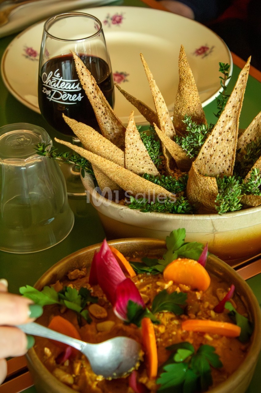 Assiette de houmous décorée de légumes colorés, accompagnée de pain pita et d'un verre de vin rouge.