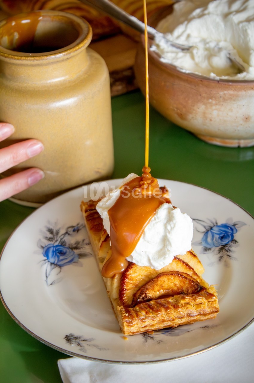 Tarte aux pommes garnie de crème fouettée, nappée de caramel liquide, servie sur une assiette décorée.