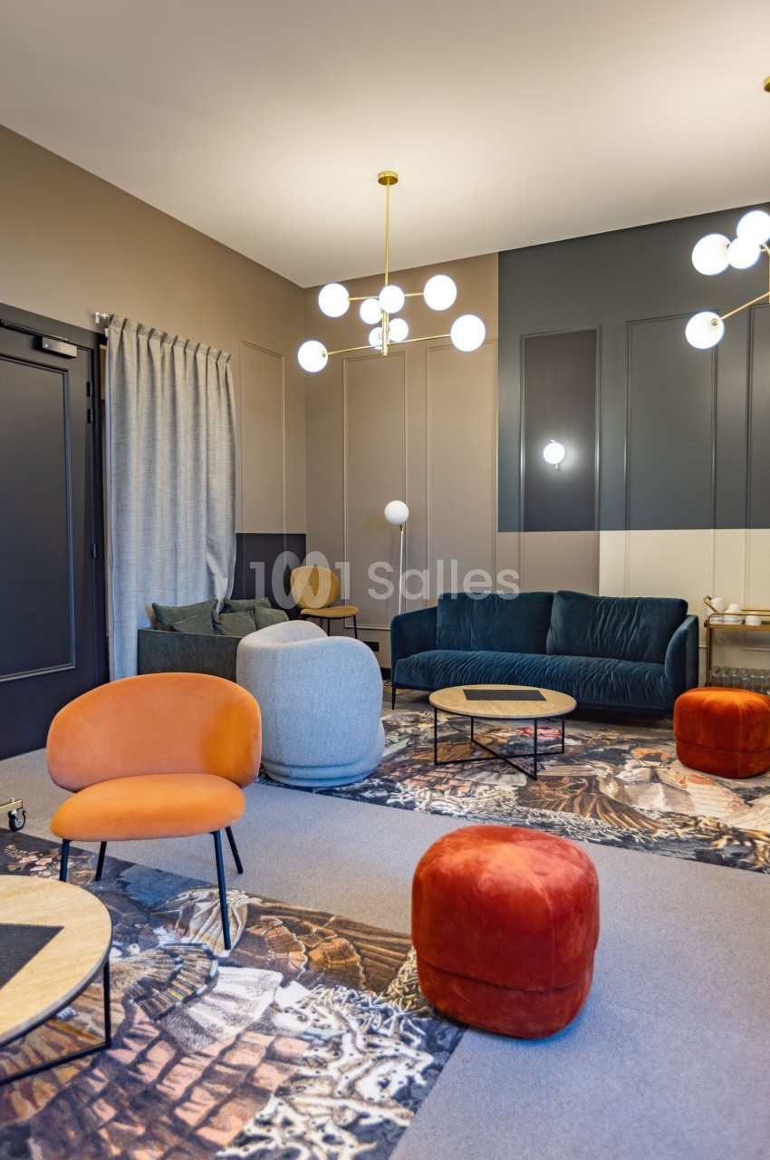 Salon moderne avec fauteuils colorés, canapé bleu, tables basses en bois et luminaires suspendus dans un décor chaleureux.