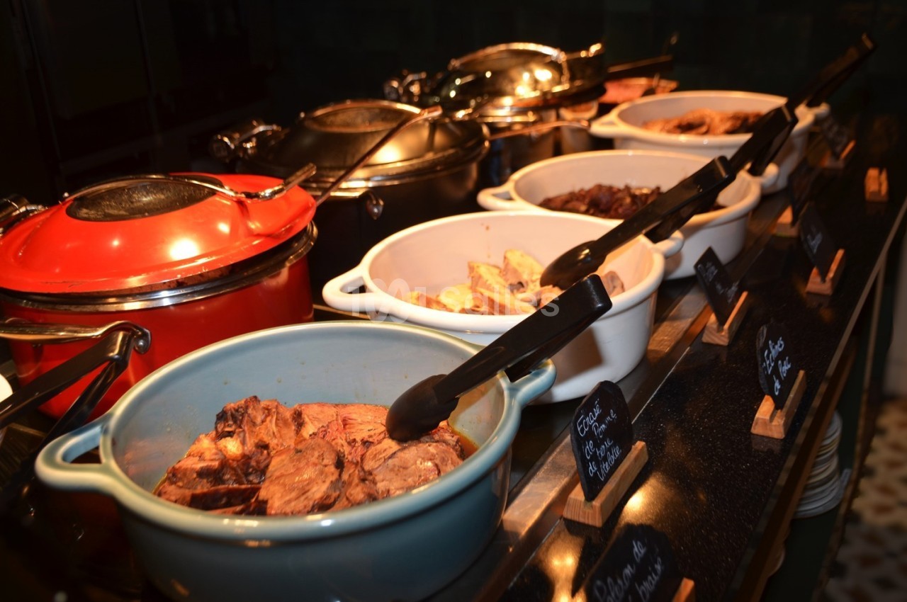 Buffet avec plusieurs plats chauds présentés dans des marmites et des plats en céramique, accompagnés de pinces.