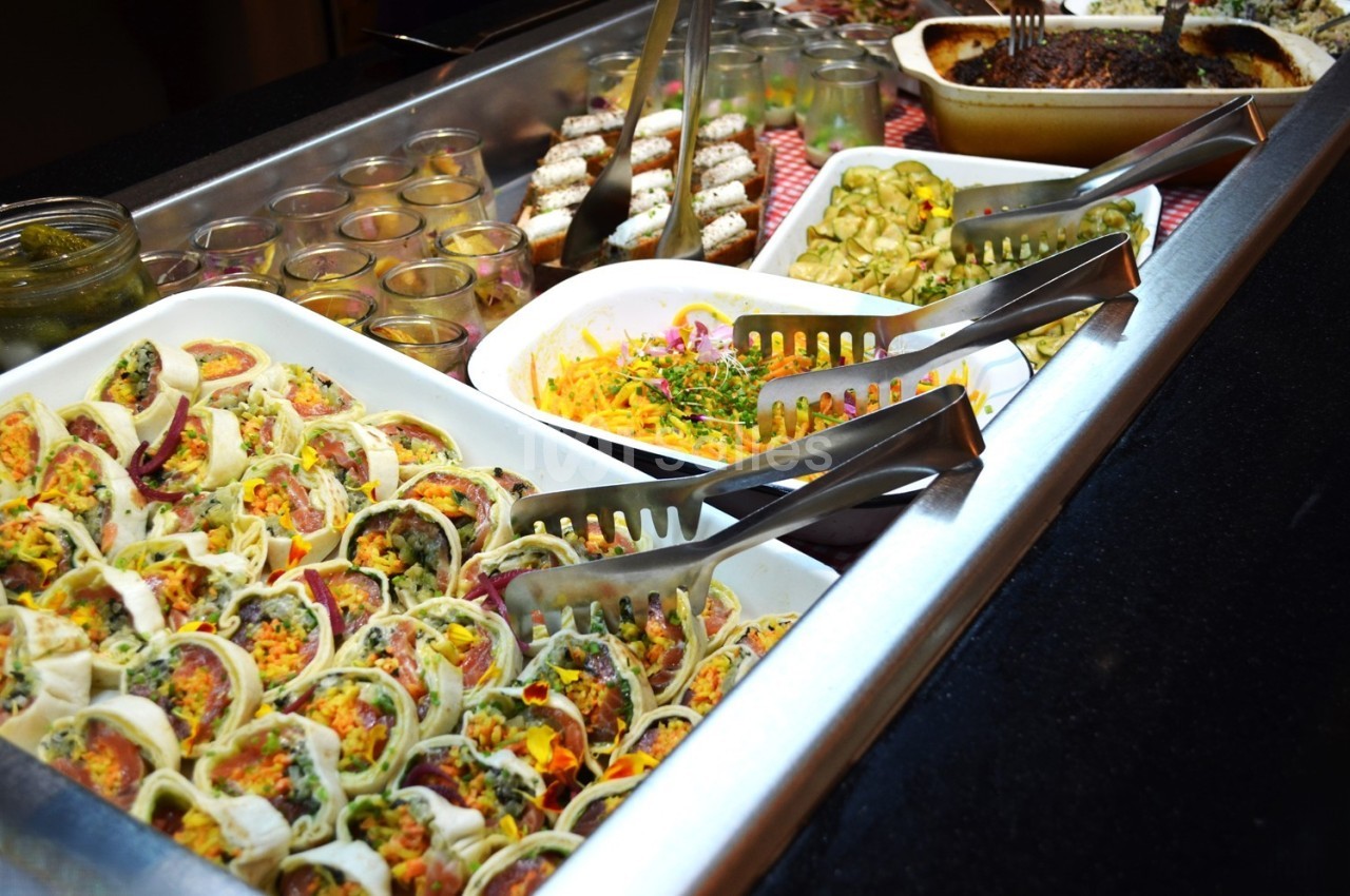 Buffet avec plats variés, incluant wraps garnis, salade colorée, gratin et desserts en arrière-plan.