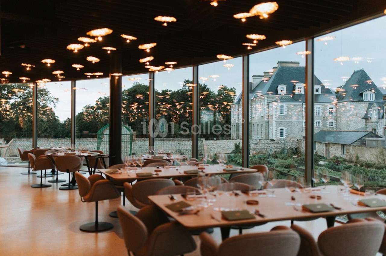Salle de restaurant moderne avec grandes baies vitrées offrant une vue sur un bâtiment historique et un jardin.