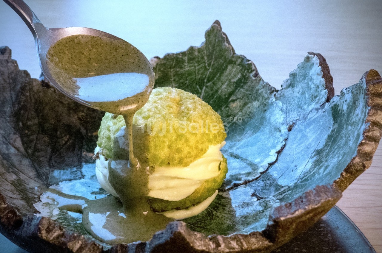 Un dessert vert avec une sauce versée à la cuillère, présenté dans une assiette en forme de feuille.