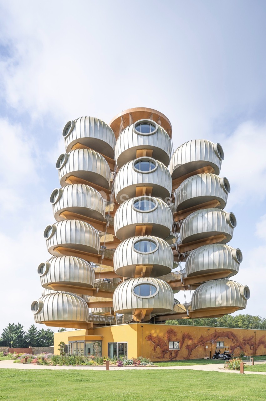Immeuble moderne avec des balcons circulaires en métal, sur une base jaune, entouré de pelouse et d'arbres.