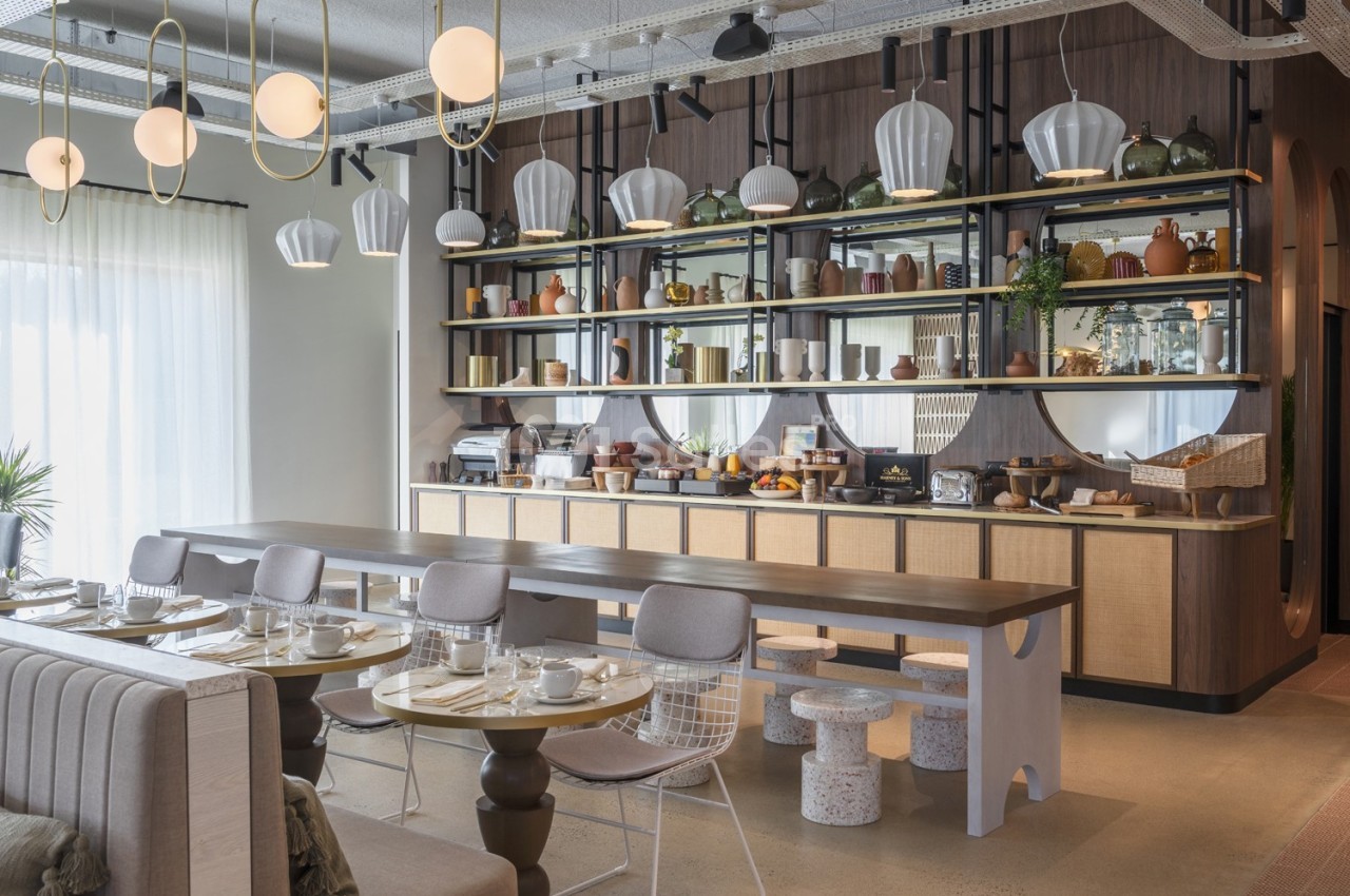 Salle de petit-déjeuner moderne avec tables dressées, buffet varié et étagères décorées de vaisselle et objets design.