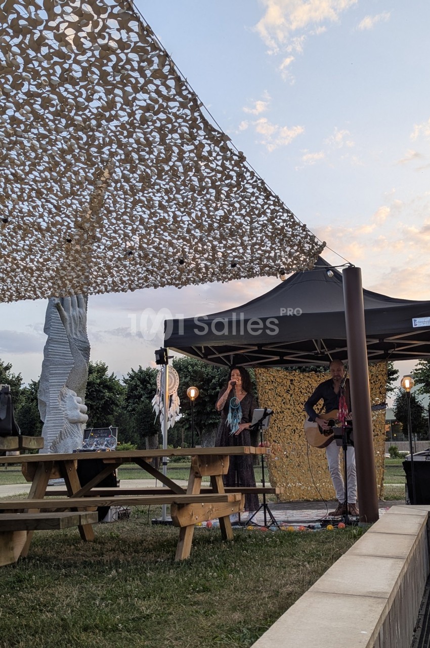 Deux musiciens jouent sous un chapiteau en plein air près de tables de pique-nique, au coucher du soleil.