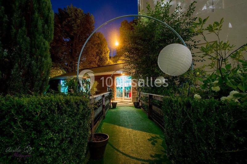 Entrée éclairée d'un bâtiment avec un chemin bordé de haies, décoré d'une arche et d'une lanterne suspendue.