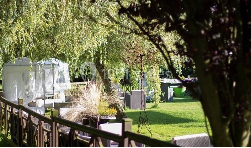 Espace extérieur verdoyant avec arbres, mobilier de jardin et tonnelle blanche sous un éclairage naturel.