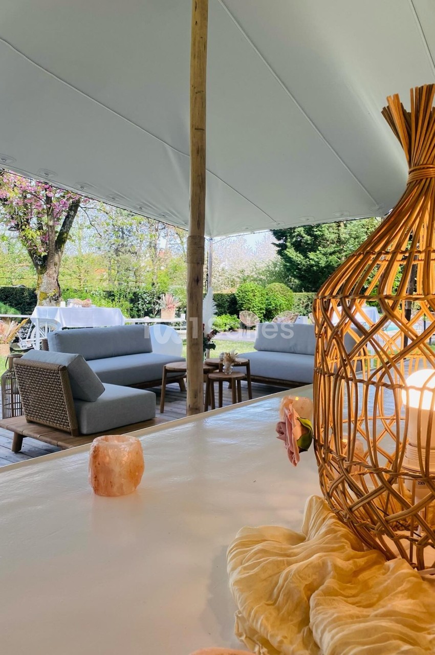 Espace extérieur aménagé avec des canapés, une table en bois et une lanterne en rotin sous une tente blanche.