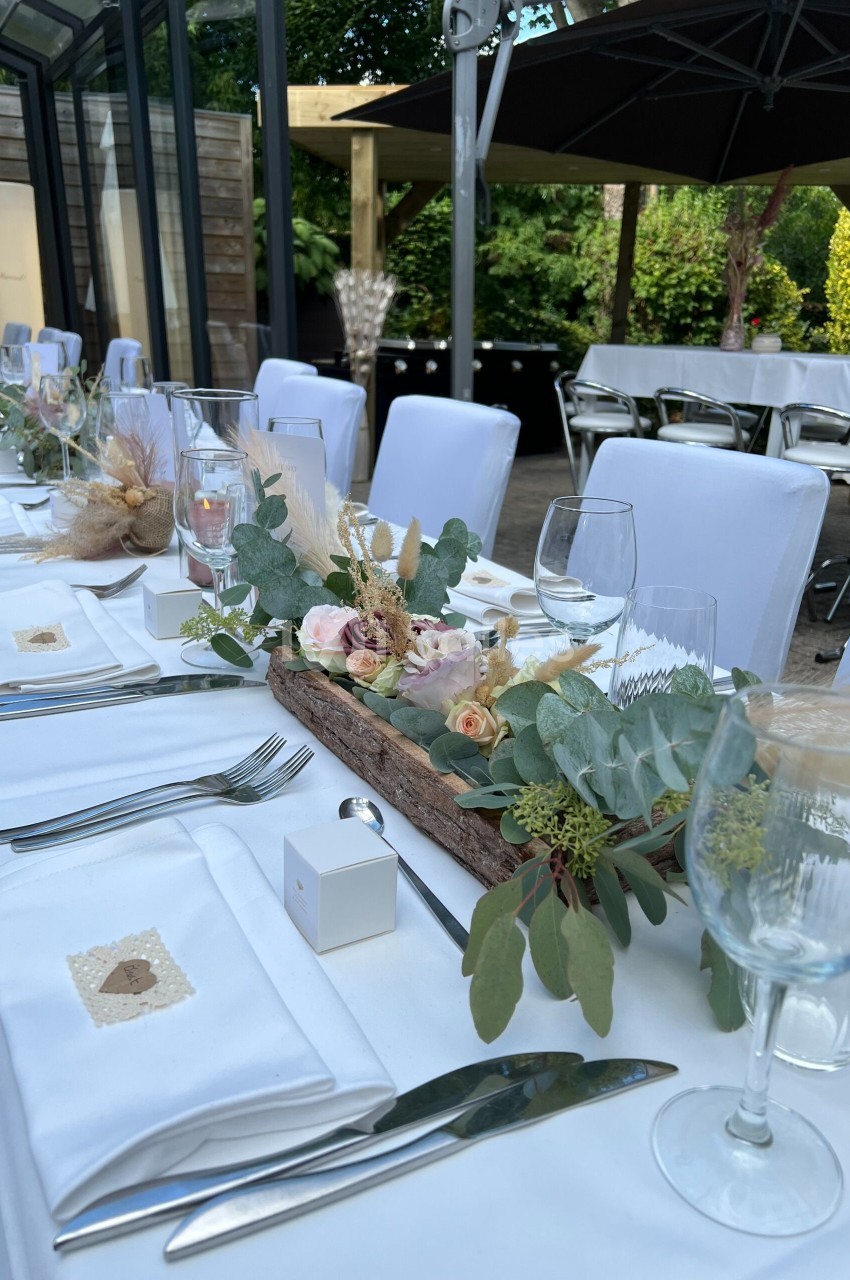 Table dressée pour un événement, décorée avec des fleurs pastel, des feuillages et des éléments naturels dans un cadre…