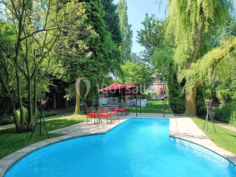 Piscine extérieure entourée de verdure avec un espace détente aménagé sous une tente rouge au fond du jardin.