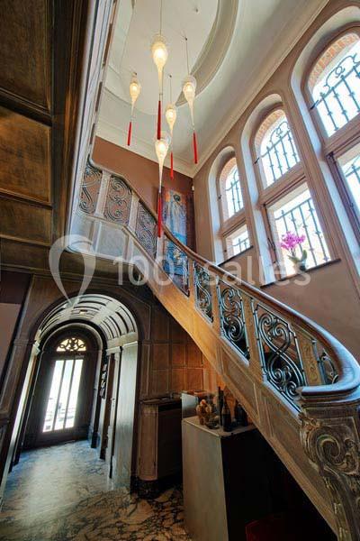Escalier en bois sculpté avec rampe en métal, éclairé par des suspensions modernes, dans un hall lumineux avec fenêtres…