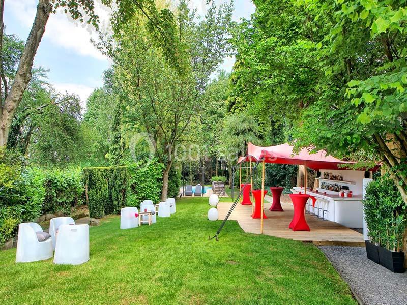 Espace extérieur aménagé avec bar, tables hautes rouges, fauteuils et verdure environnante.