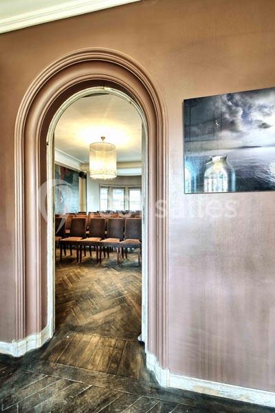 Vue d'une salle avec des chaises alignées, visible à travers une porte en arche dans un intérieur aux tons chauds.