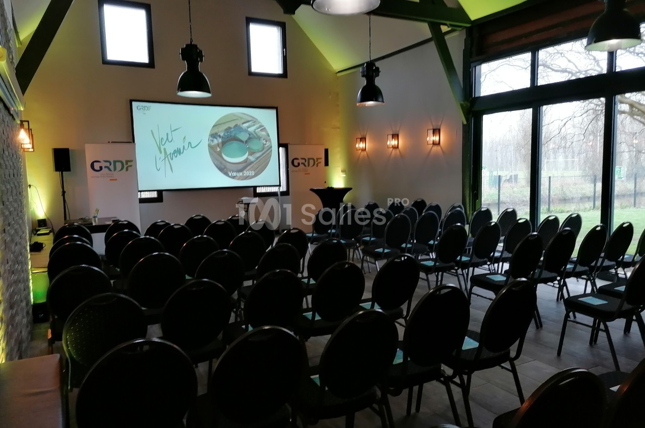 Salle de conférence aménagée avec des rangées de chaises, un écran de projection allumé et des logos GRDF visibles.