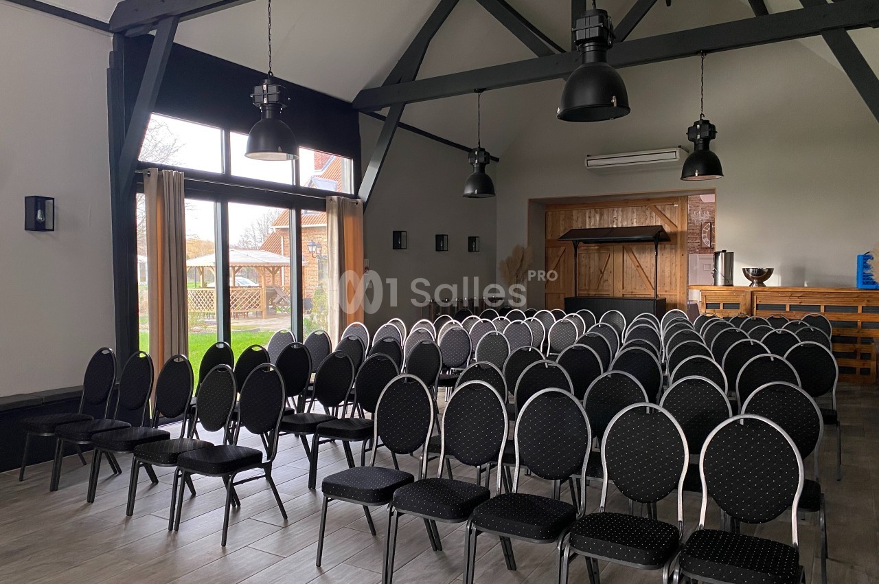 Salle de réunion lumineuse avec des rangées de chaises noires alignées face à une grande baie vitrée.