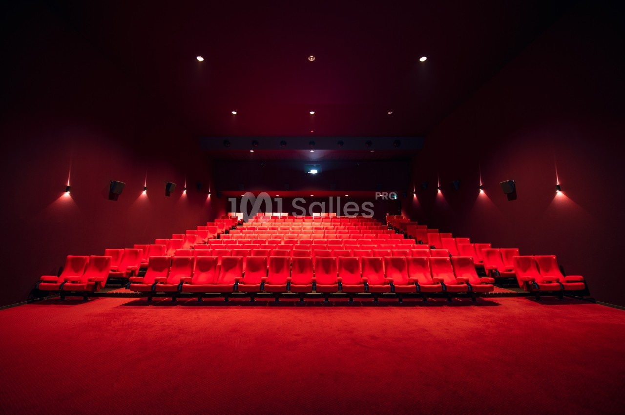 Salle de cinéma vide avec des rangées de sièges rouges et un éclairage tamisé.