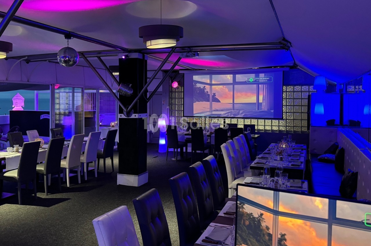 Salle de restaurant moderne avec éclairage violet, grandes baies vitrées et vue sur un coucher de soleil.