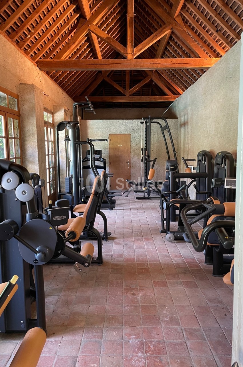 Salle de sport avec équipements de musculation modernes, sol en briques et plafond en bois.
