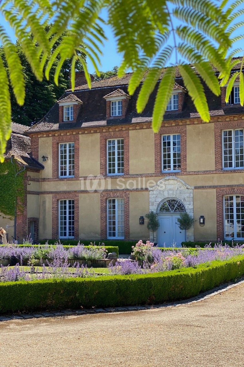 Façade d'une maison de campagne en pierre entourée de lavande et de haies, sous des branches de fougère.