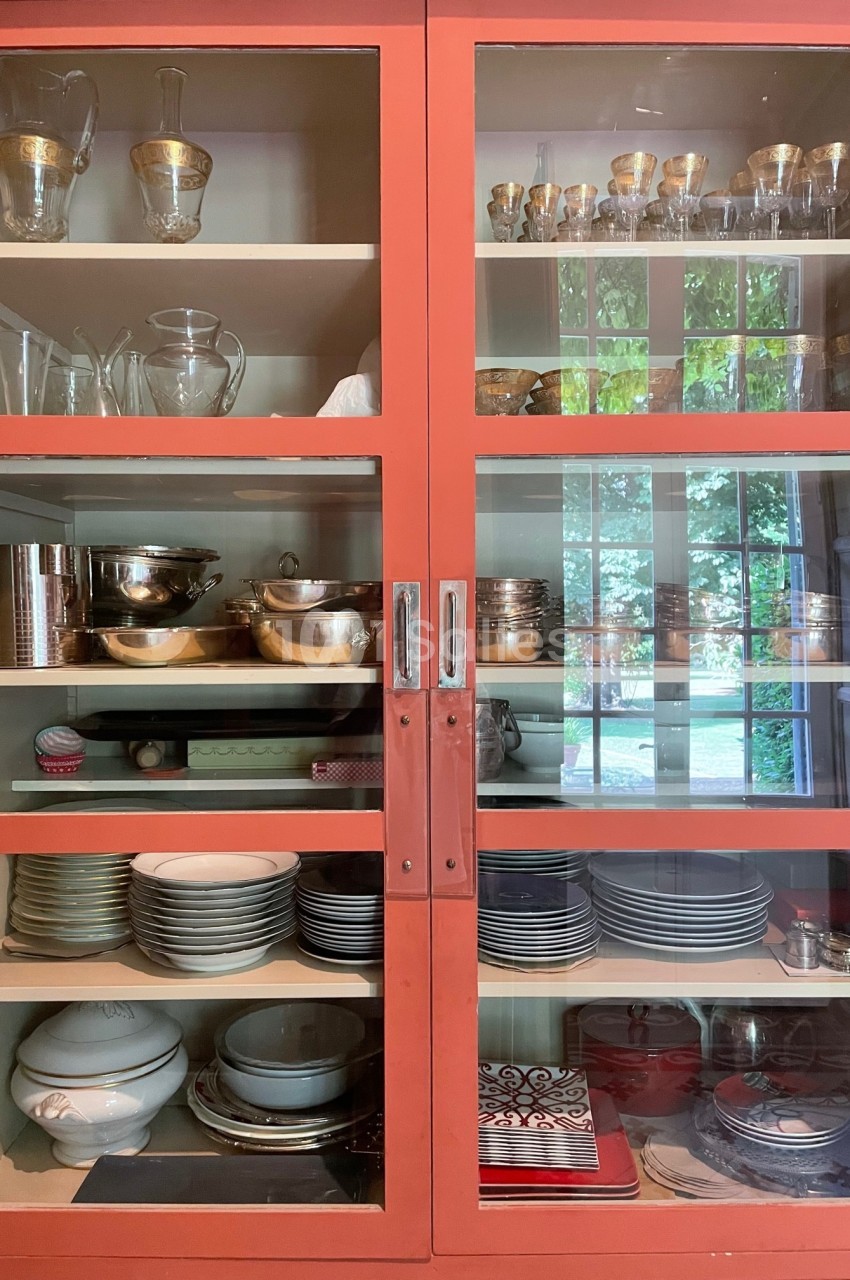 Vaisselier rouge avec portes vitrées, contenant des verres, plats, bols et assiettes en céramique et en métal.