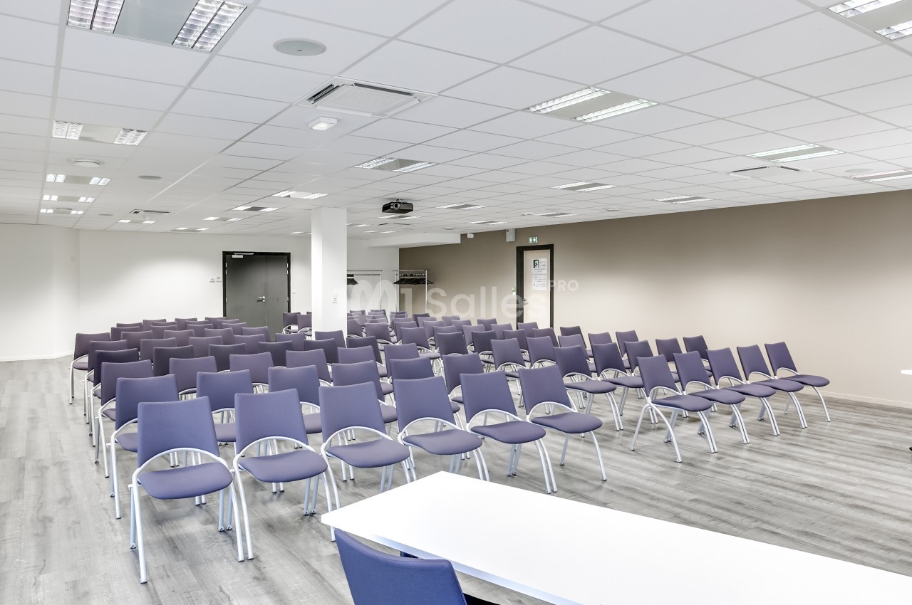 Salle de conférence lumineuse avec des rangées de chaises violettes alignées face à une table blanche.