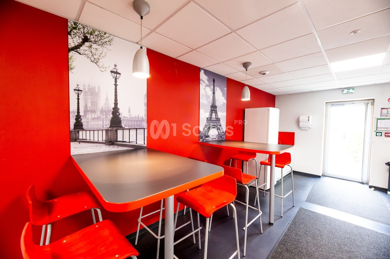 Salle de pause avec tables hautes, chaises rouges, murs rouges et décorations murales représentant Paris.