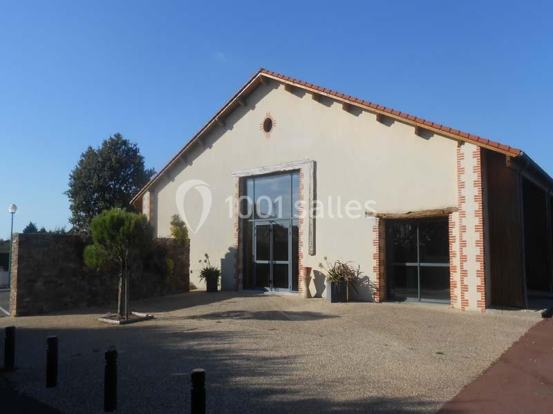 Bâtiment moderne avec façade claire, toit en tuiles rouges et entrée vitrée, entouré d'arbres et d'un espace pavé.