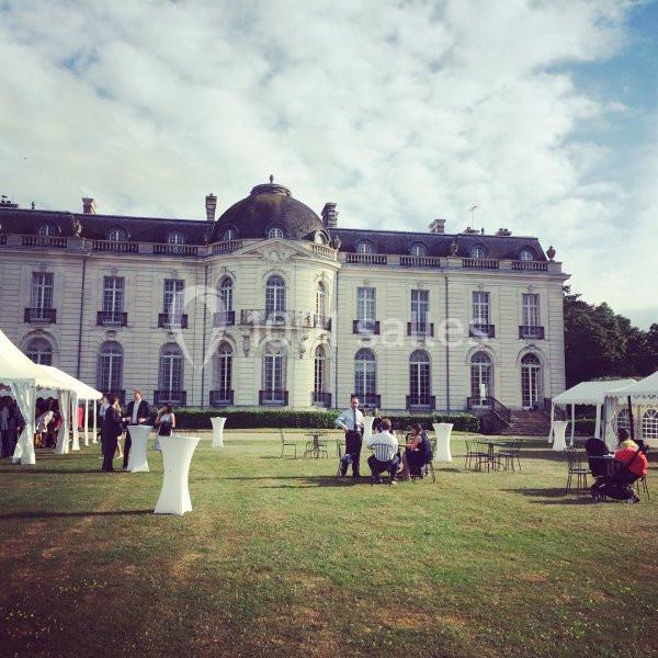 Façade d'un château entouré de pelouses, avec des tentes blanches et des personnes assises ou debout.