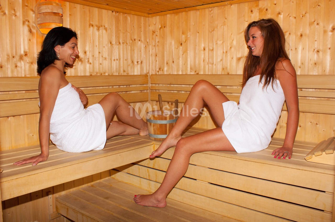 Deux femmes en serviettes discutent et se détendent dans un sauna en bois lumineux.