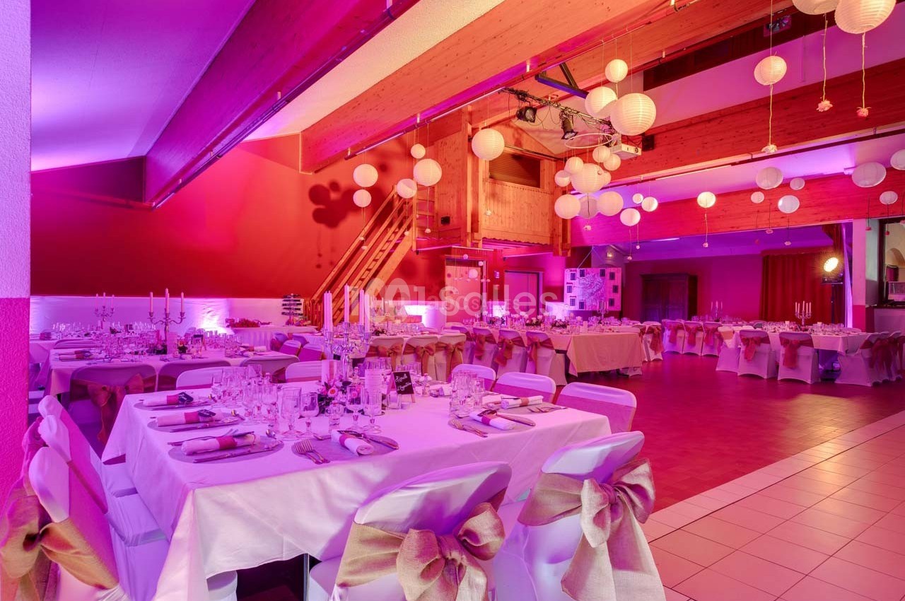 Salle de réception décorée avec des tables dressées, des nappes blanches et des lanternes suspendues au plafond.