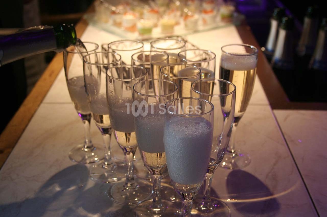Flûtes de champagne remplies sur une table, avec une bouteille versant dans l'une d'elles au premier plan.