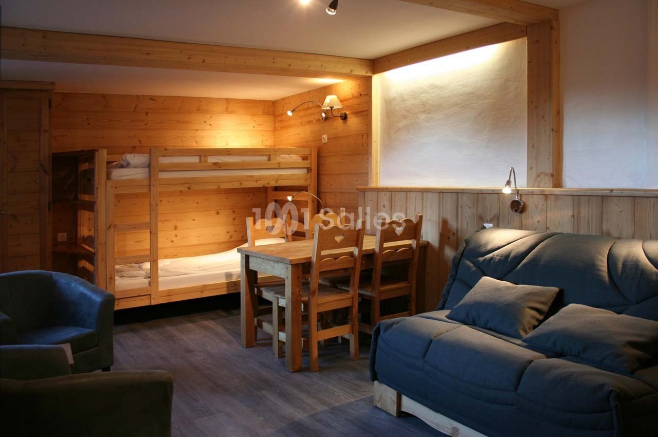 Salon en bois avec canapé, table à manger, chaises, lits superposés et éclairage chaleureux.