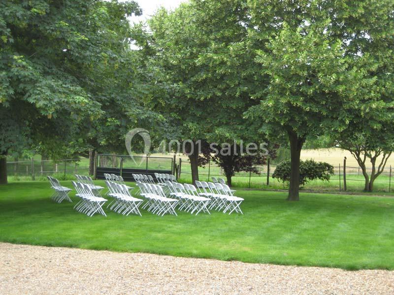 Chaises blanches disposées en rangées sur une pelouse verte, à l'ombre d'arbres dans un cadre extérieur.