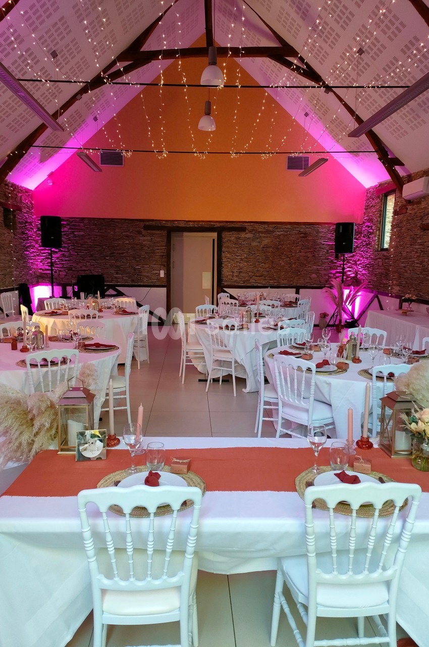 Salle de réception décorée avec des tables dressées, des guirlandes lumineuses suspendues et un éclairage rose.