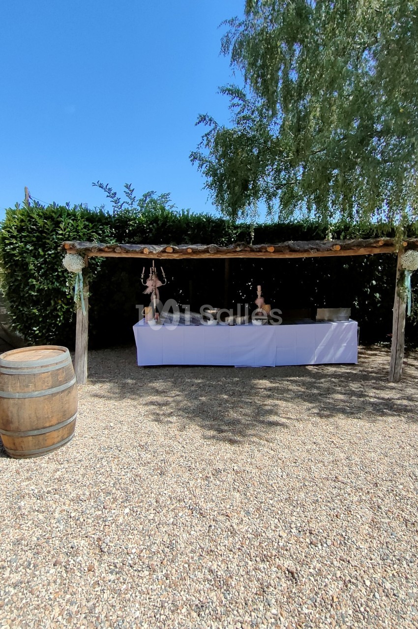Table de buffet décorée sous une pergola en bois, entourée de verdure, avec un tonneau en premier plan.