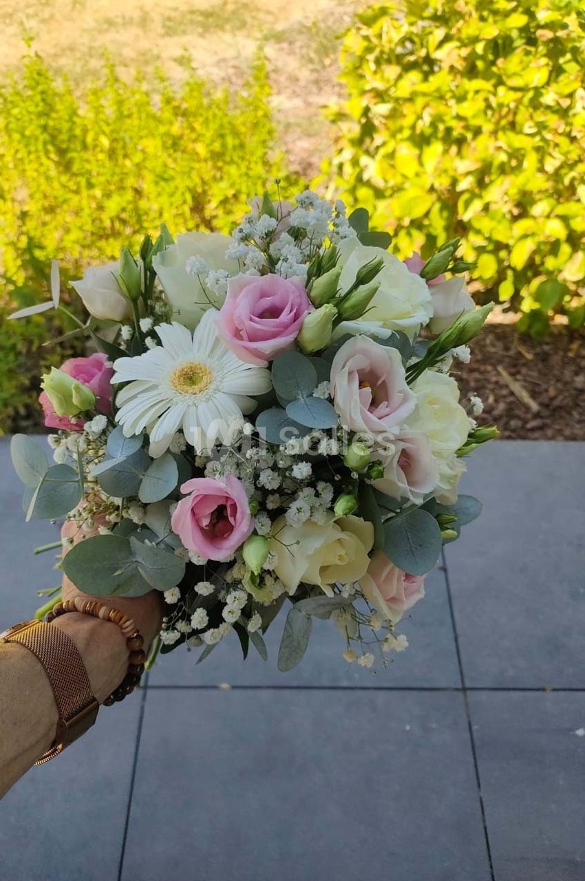 Bouquet de fleurs pastel avec roses, gerbera blanc, gypsophile et feuillage, tenu à la main en extérieur.
