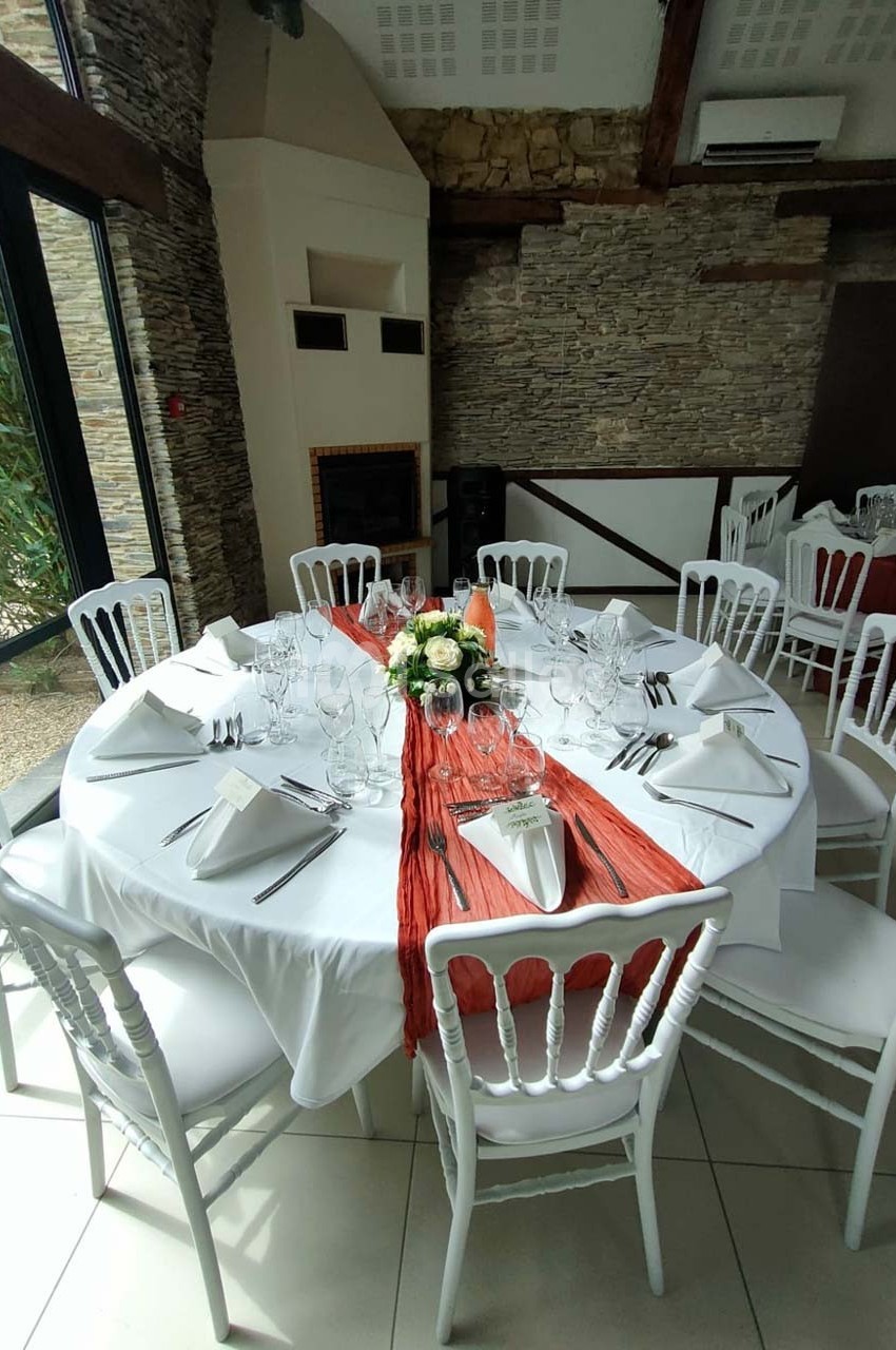 Table ronde dressée pour un repas, avec nappe blanche, chemin de table rouge, vaisselle élégante et centre floral.