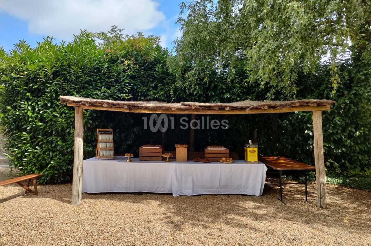 Table en extérieur sous un abri en bois, dressée avec des plats et des boîtes, entourée de végétation.