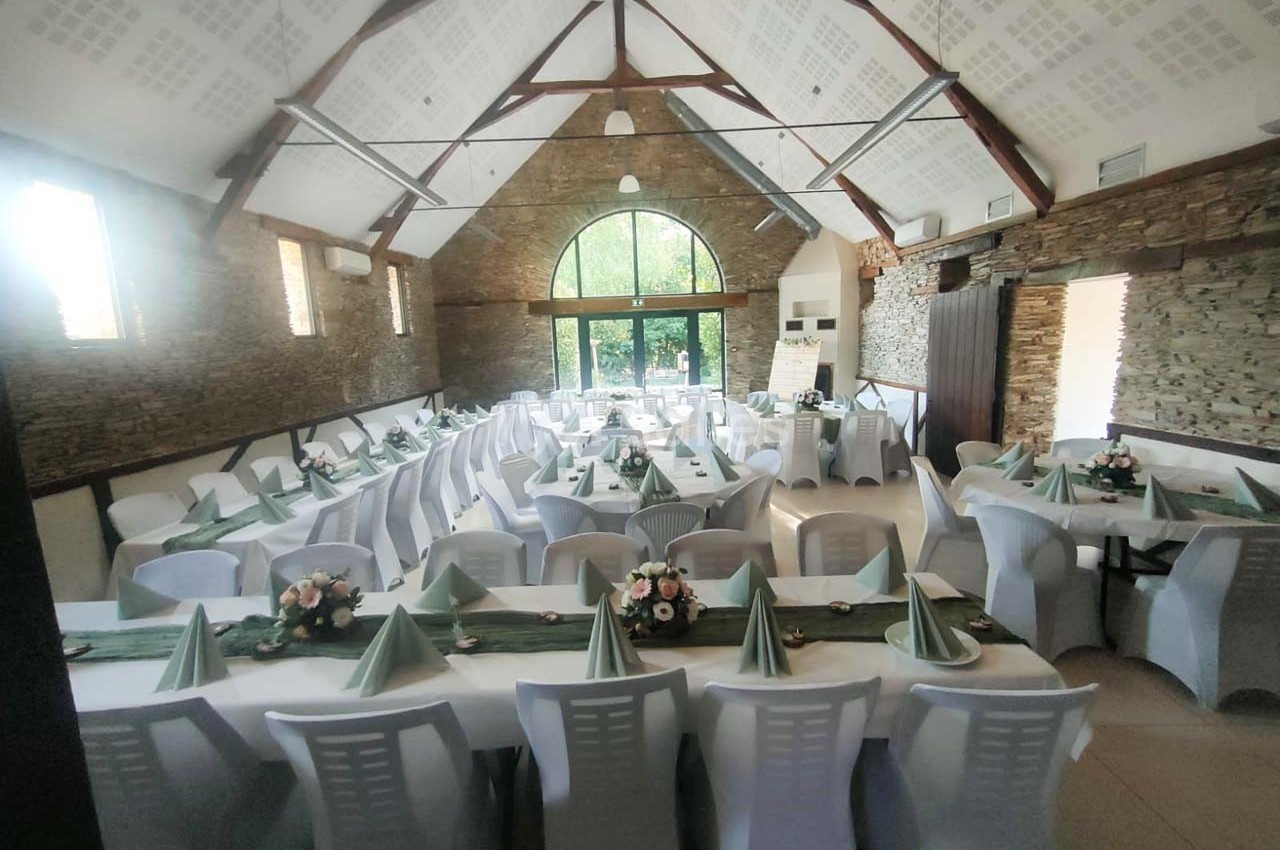 Salle de réception avec tables dressées, nappes blanches, serviettes vertes pliées et décorations florales.