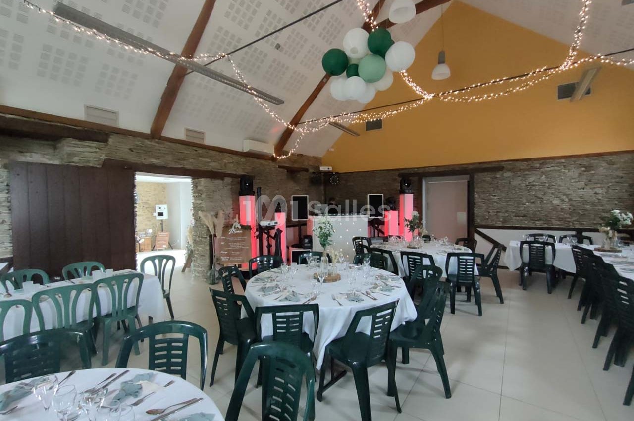 Salle de réception décorée avec des tables rondes dressées, des chaises vertes et des guirlandes lumineuses suspendues.