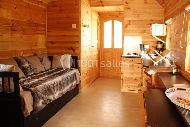 Intérieur d'un chalet en bois avec un lit, une kitchenette équipée et une table en bois près d'une fenêtre.