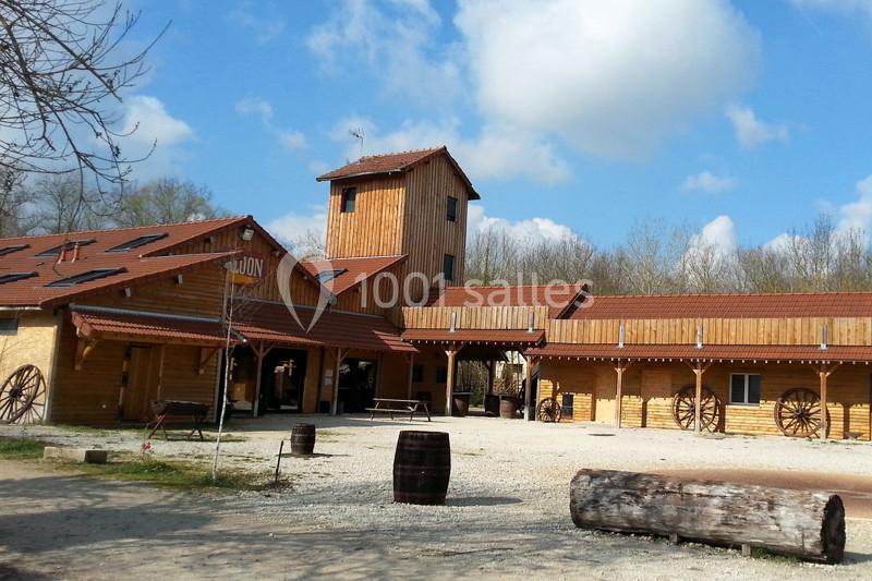 Bâtiment en bois de style ranch avec une tour centrale, entouré de végétation et d'éléments décoratifs rustiques.