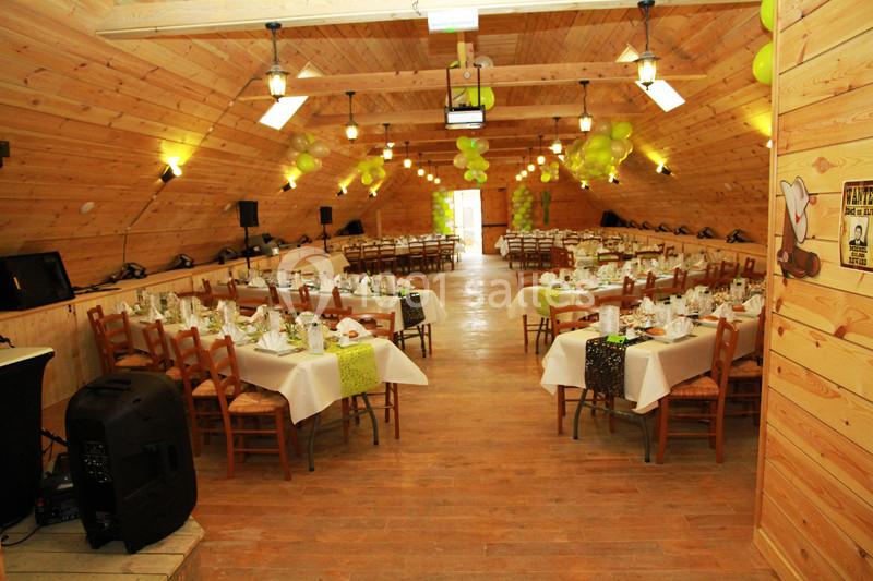 Salle en bois décorée avec des ballons verts, tables dressées pour un événement avec nappes blanches et chaises en bois.