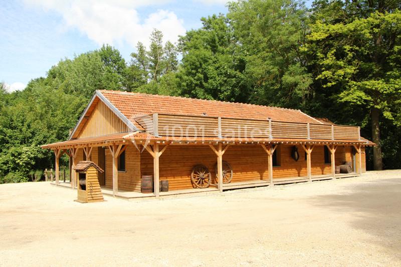 Bâtiment en bois avec toit en tuiles, entouré de végétation, et décoré de roues de charrette.