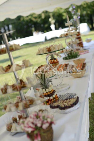 Buffet en plein air avec des présentoirs garnis de bouchées apéritives, fruits et desserts sur une table blanche.