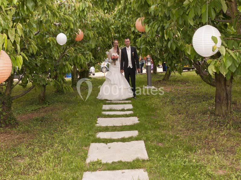 Un couple en tenue de mariage marche sur un chemin de dalles entouré d'arbres décorés de lanternes.